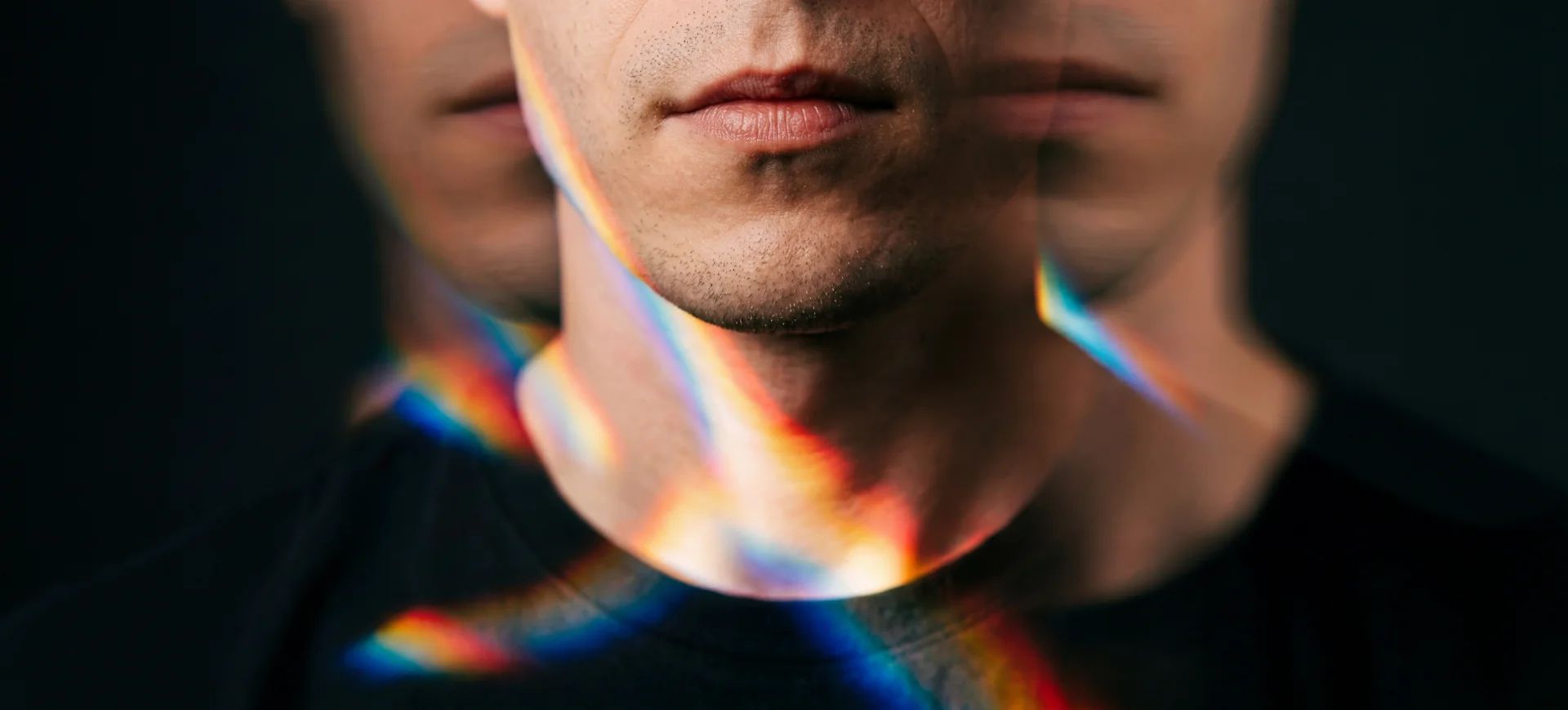 Close-up of a man's face, blurred in motion, with rainbow light reflections on his neck.