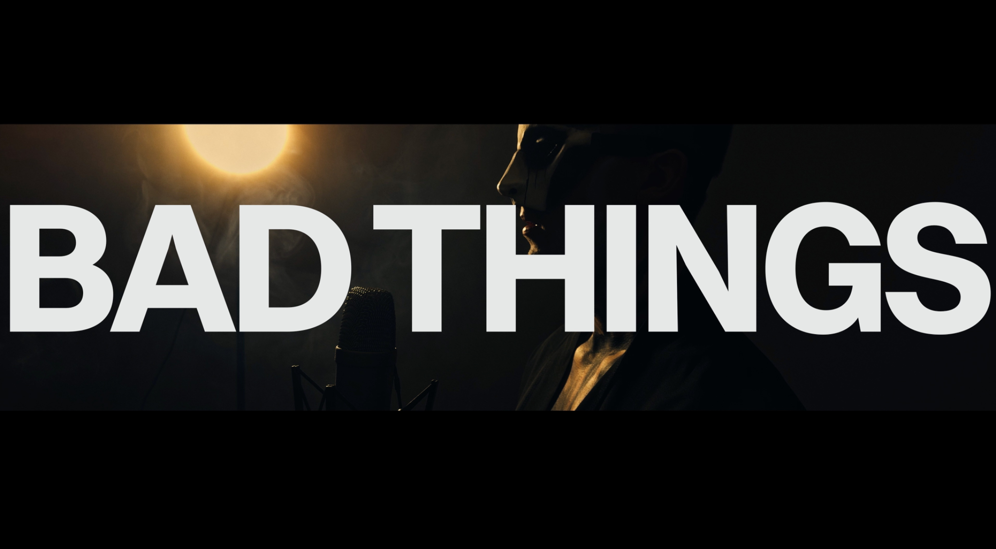 "BAD THINGS" in white text over a person at a microphone bathed in light and smoke.