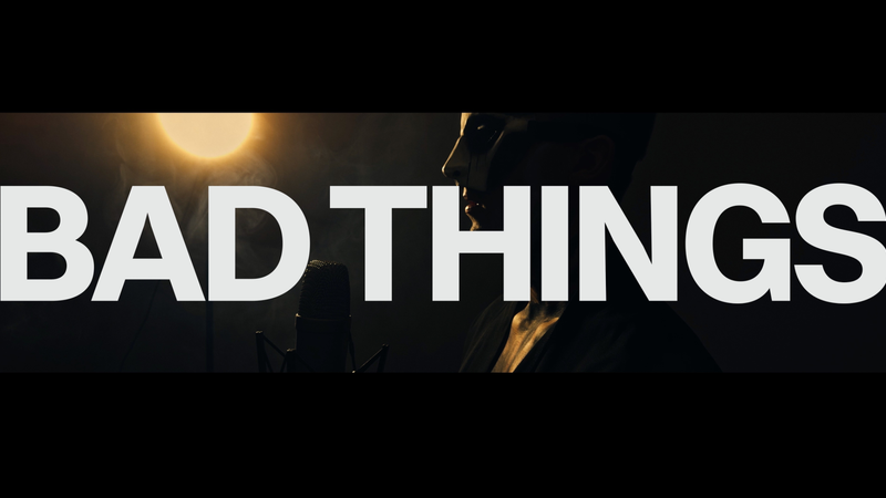 "BAD THINGS" in white text over a person at a microphone bathed in light and smoke.