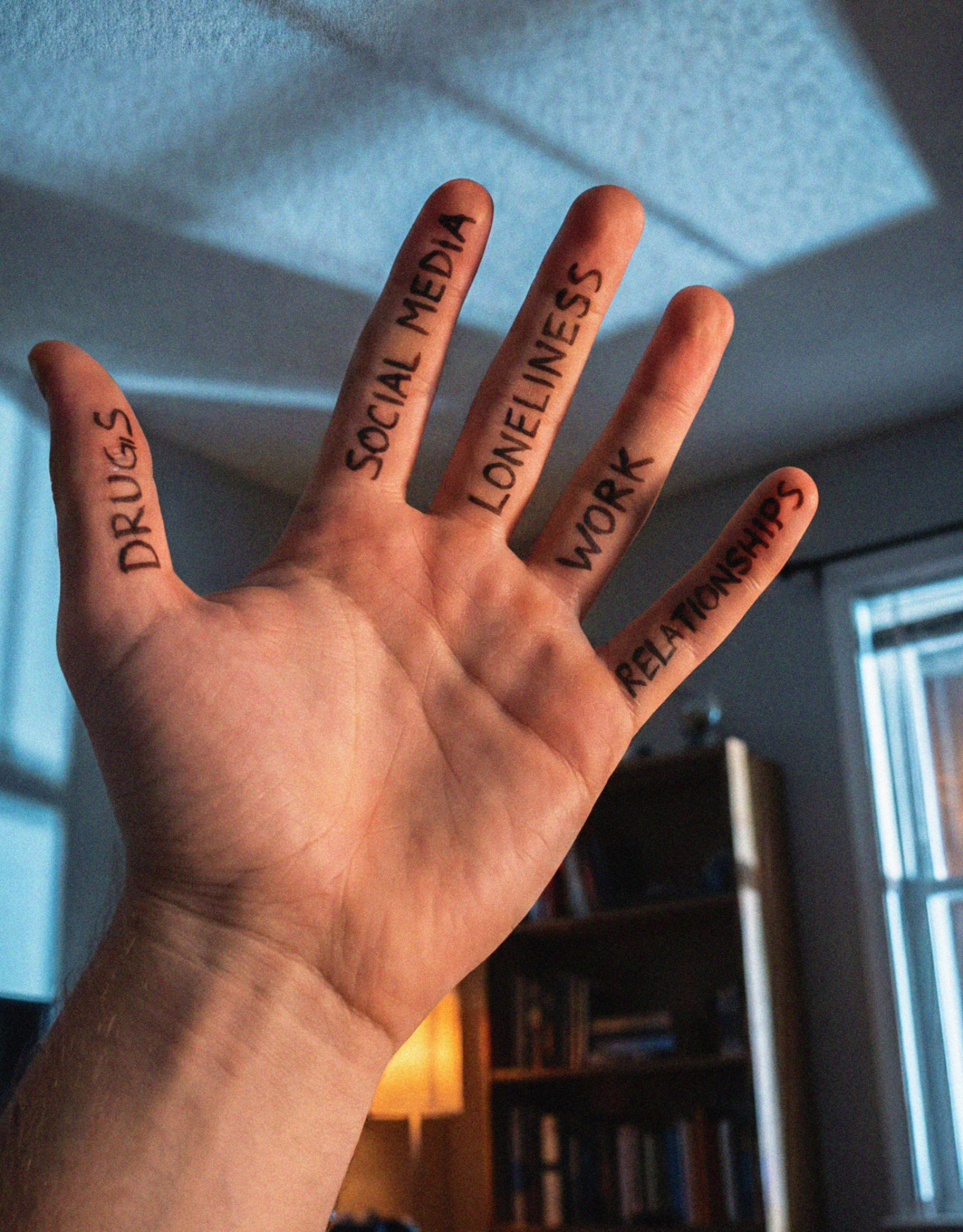 Hand with "Drugs," "Social Media," "Loneliness," "Work," and "Relationships" written on fingers.